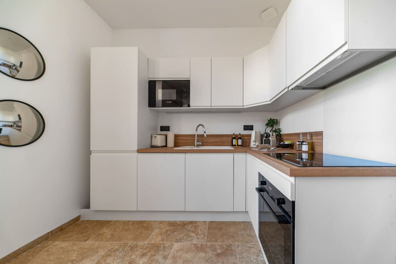 A modern kitchen with white cabinets, a wooden countertop, a microwave, and a sink.