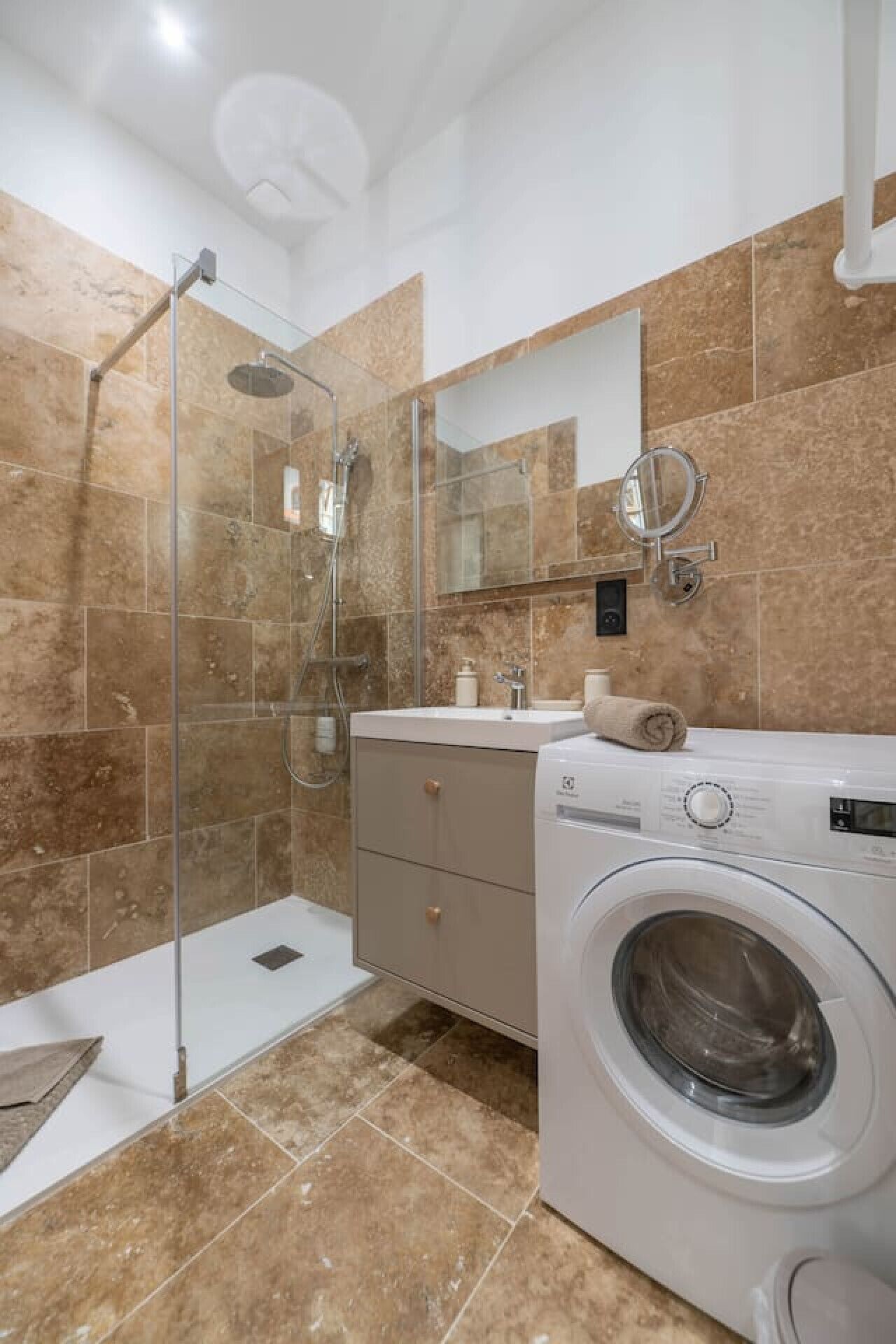 Un baño moderno con ducha envuelta en vidrio, lavadora integrada y tocador con espejo.