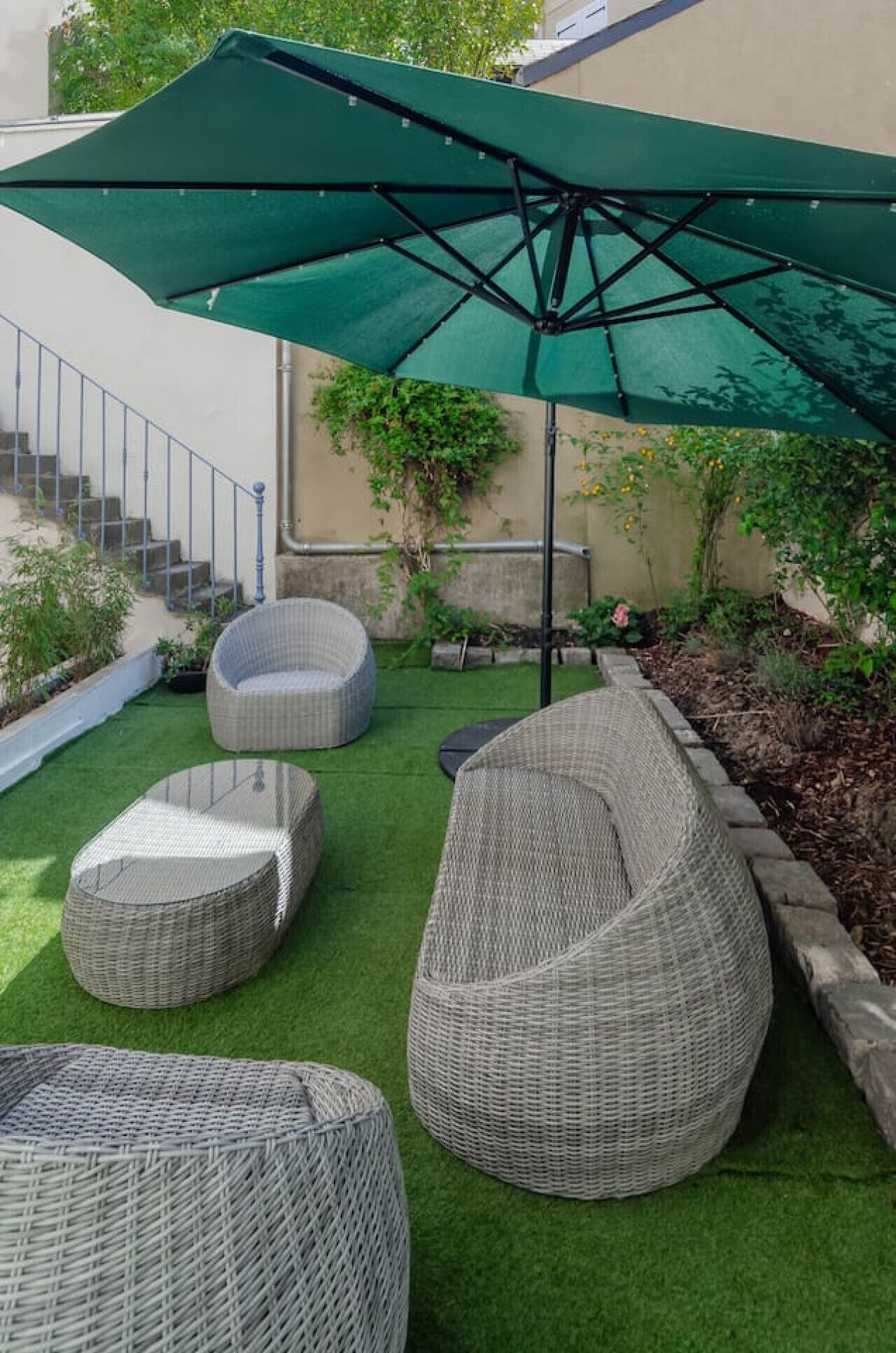 Une terrasse avec des meubles en osier, un parasol vert et un escalier.