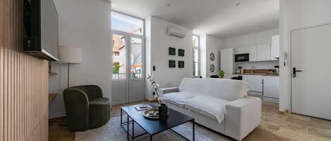 Ein modernes Wohnzimmer mit einem weißen Sofa, einem schwarzen Couchtisch und einem grünen Sessel. Im Hintergrund ist eine Küchenzeile erkennbar.
