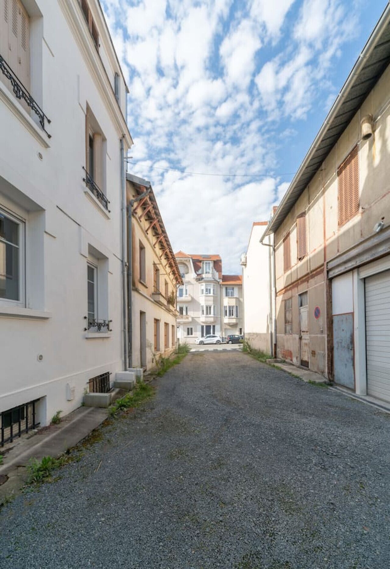 Una calle estrecha flanqueada por edificios, un camino de grava y cielo despejado.
