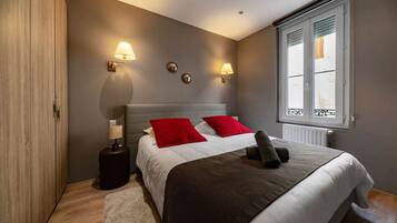 A bedroom with a bed, two bedside lamps, a window with blinds, and a radiator.