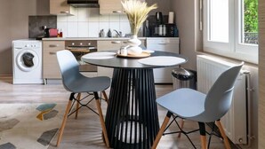 A modern kitchen with a central island, two chairs, a washing machine, and a large window.