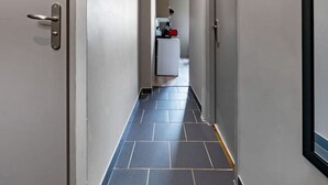 A corridor with a tiled floor, doors on both sides, and a kitchenette area in the distance.