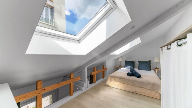 Een slaapkamer met dakraam, houten balken, een bed en een nachtkastje.