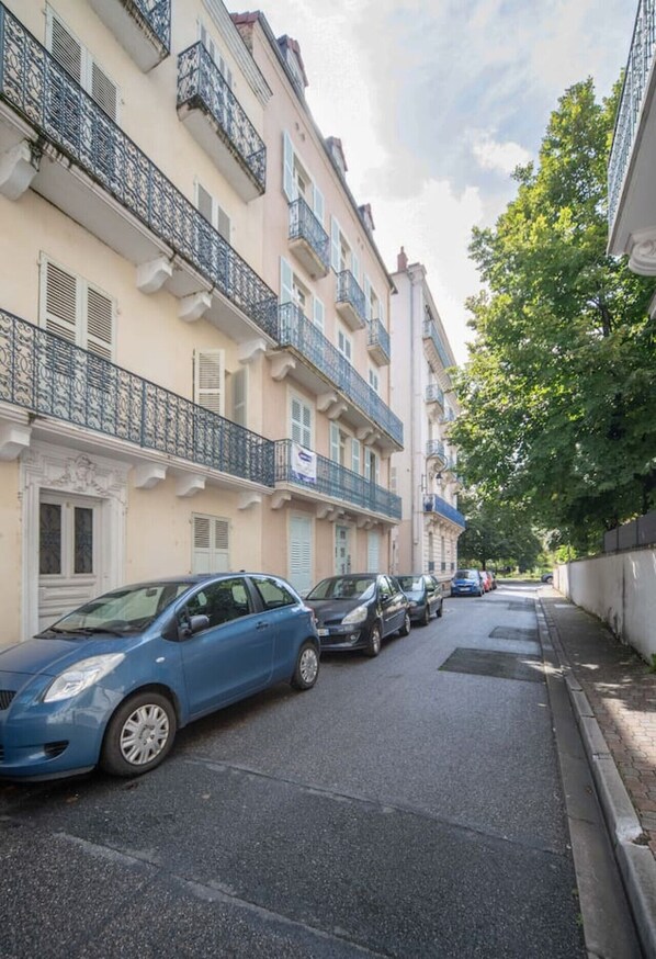 Una calle estrecha flanqueada por edificios de varios pisos, con balcones y barandillas metálicas.