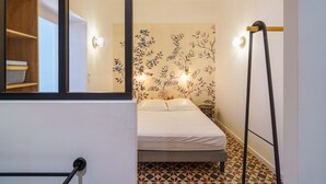 Une chambre à coucher de taille réduite, comprenant un lit, un miroir, un luminaire suspendu et un revêtement de sol à motifs.
