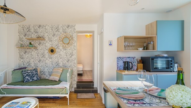 Un espace de vie compact comprenant un canapé, une petite table, un coin cuisine avec un four à micro-ondes et un escalier menant à une pièce adjacente.