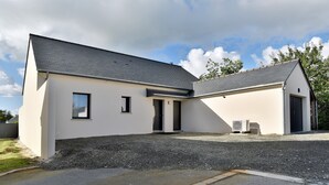 A modern two-story building with a sloped roof, a gravel driveway, and a small outdoor area with an air conditioning unit. - Cancale à la plage - Maison avec terrasse pour 6 (Cancale)