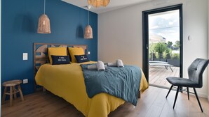 A bedroom with a bed, two hanging lamps, a chair, and a view of the outside. - Cancale à la plage - Maison avec terrasse pour 6 (Cancale)