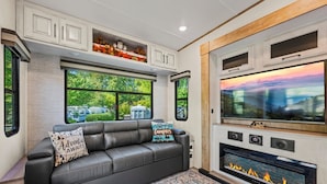 Interior moderno de autocaravana con sofá de cuero, chimenea y televisor grande.