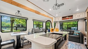 Interior moderno de autocaravana con isla de cocina, zona de estar y ventanas amplias que ofrecen vistas panorámicas.