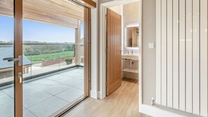 A modern bathroom with a glass door leading to a balcony, a wooden door, and a white vanity with a mirror. - Hollyhocks - UK47975 (Woodford)