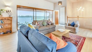 A spacious living room with a large sofa, a coffee table, and a view of the sea through large windows. - Hollyhocks - UK47975 (Woodford)