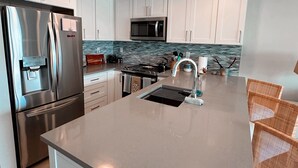 Una cocina moderna con armarios blancos, un refrigerador de acero inoxidable, un microondas y una isla grande con un fregadero.