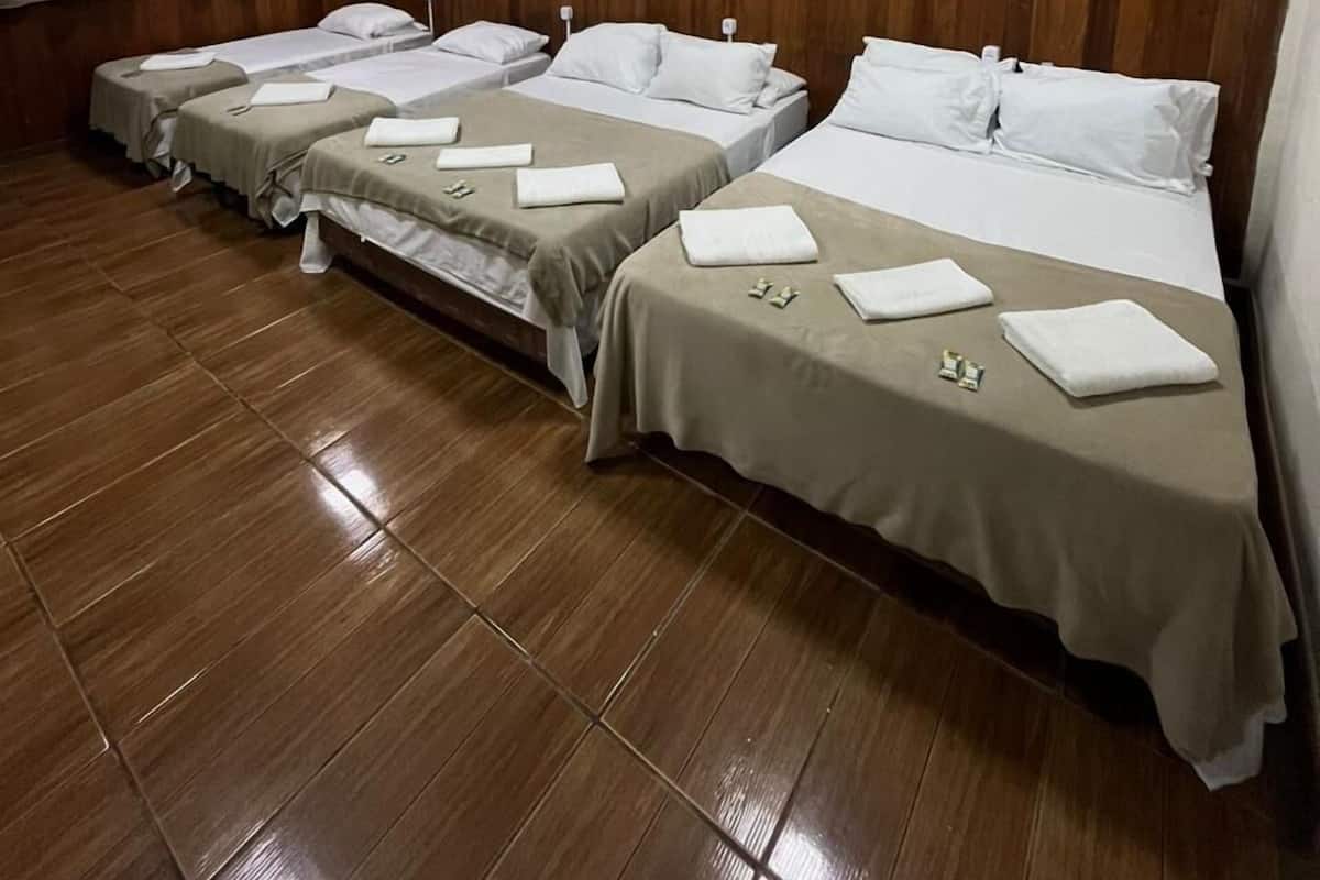 A hotel room with four beds arranged in a row, wooden panel walls, and a painting on the wall.
