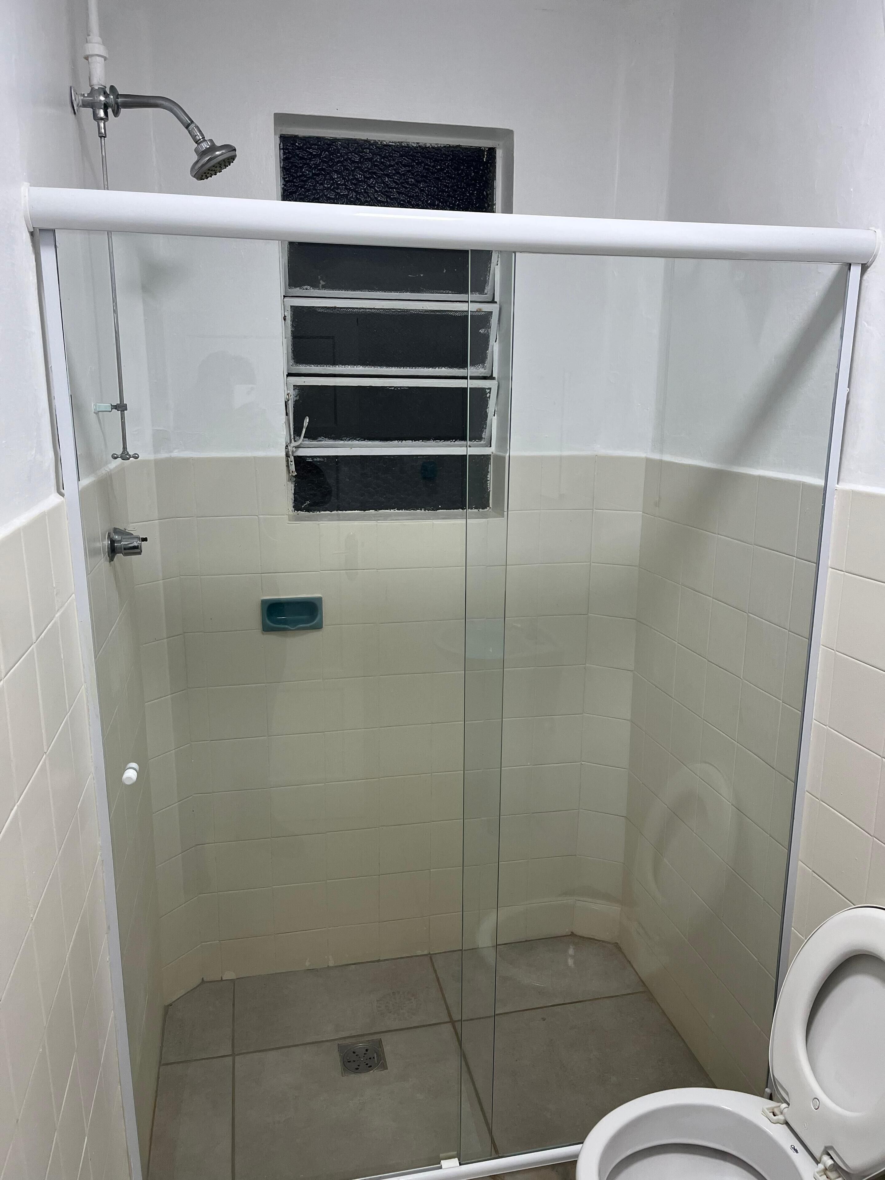 Um chuveiro pequeno e fechado, com porta de vidro, janela e vaso sanitário.