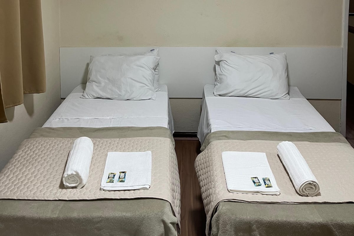 A hotel room with two beds, beige walls, and curtains.