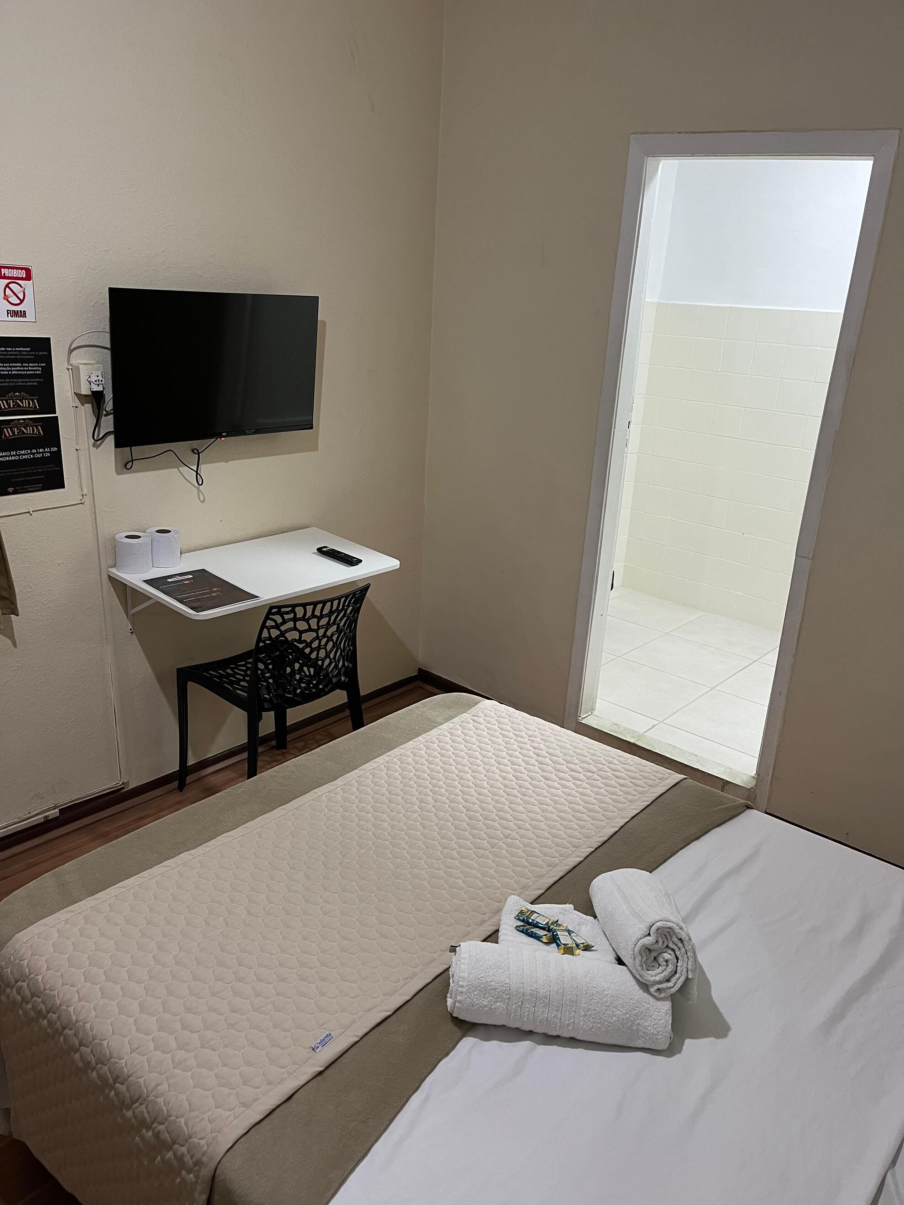 Una habitación de hotel con cama, escritorio, silla, televisor y ventana.
