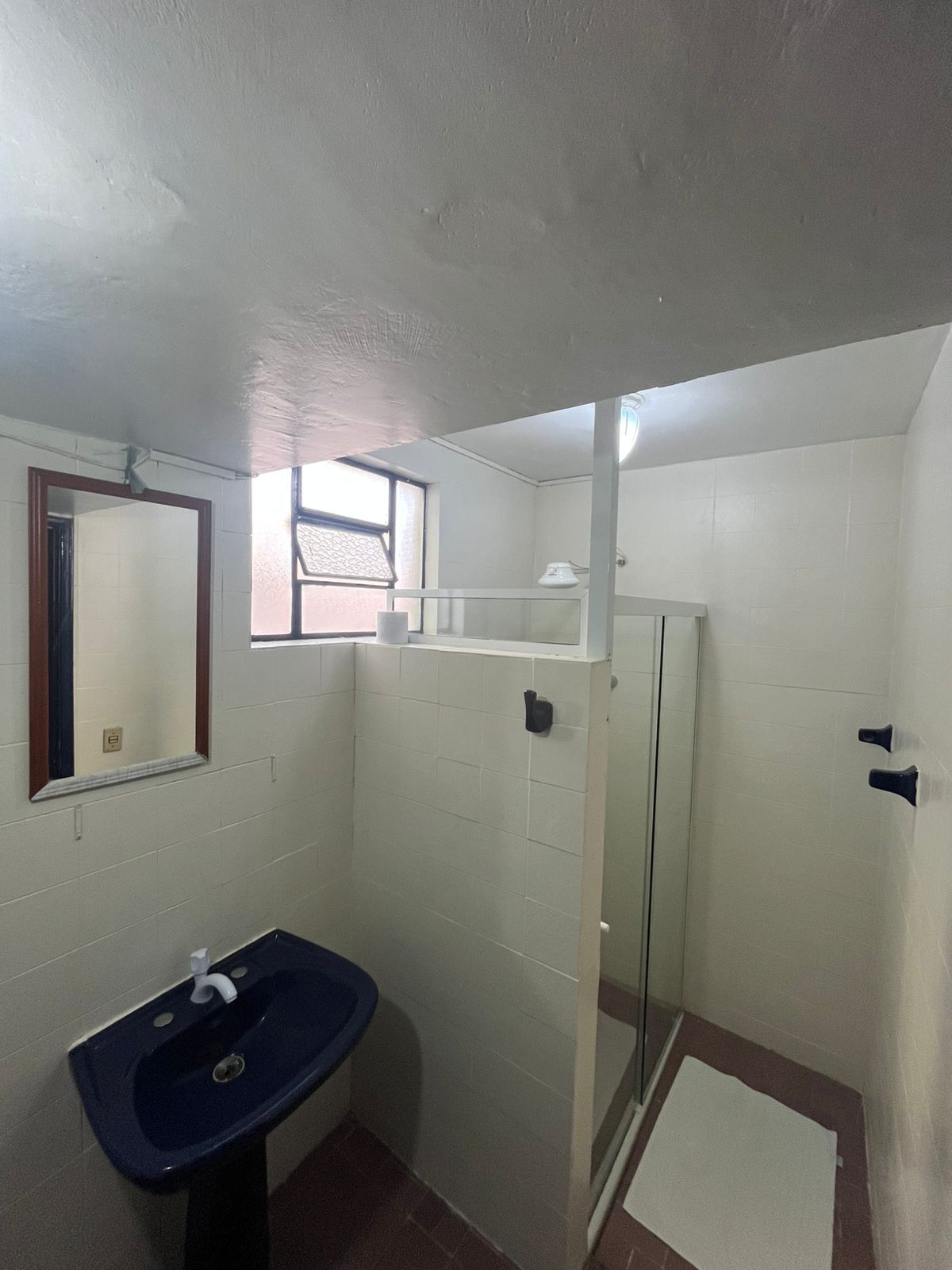 Un baño con un lavabo azul, un espejo, una ventana y una zona de ducha.