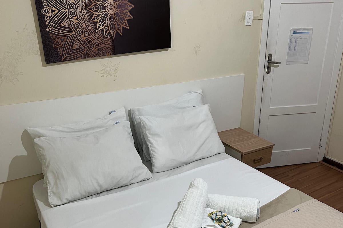 A neatly made bed with white linens, a decorative wall piece, and a door with a notice.