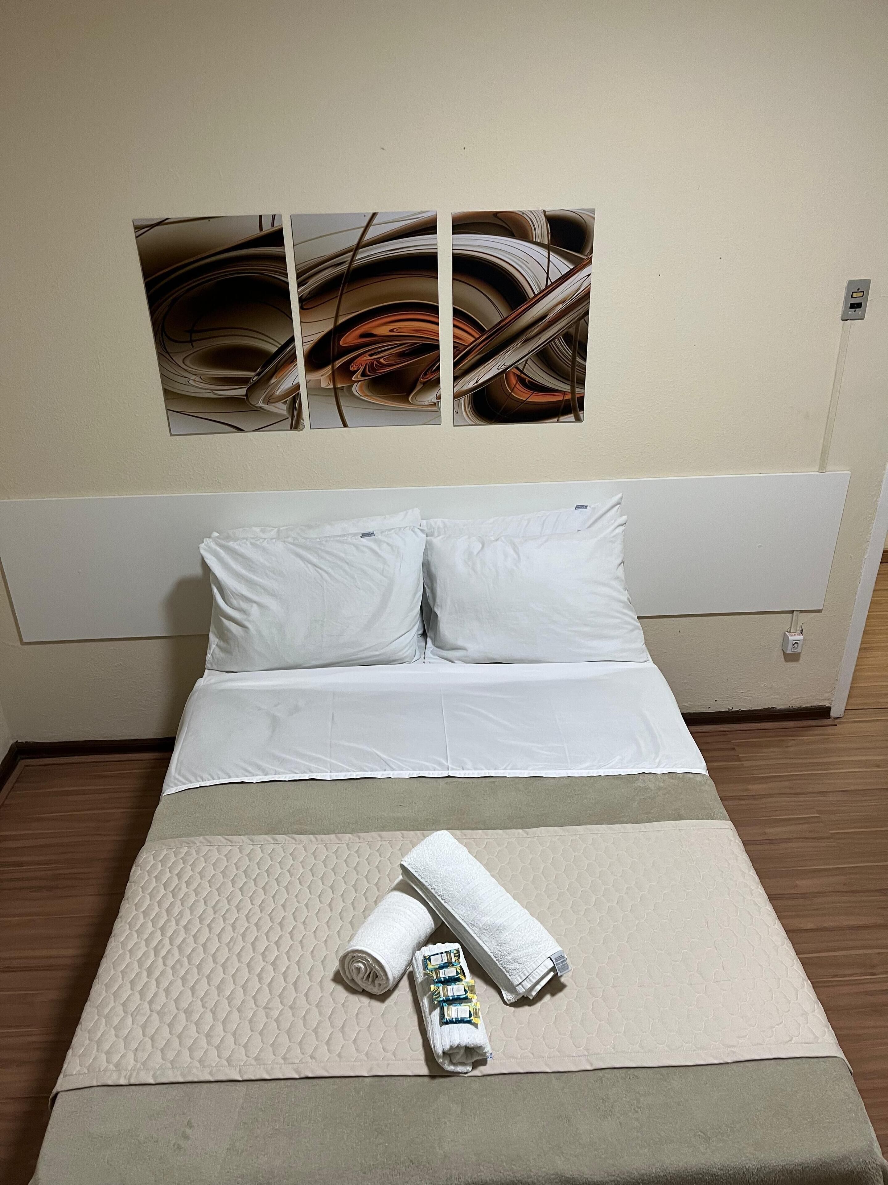 Una cama bien hecha con ropa blanca, un colchón acolchado y una toalla enrollada con un objeto amarillo encima.