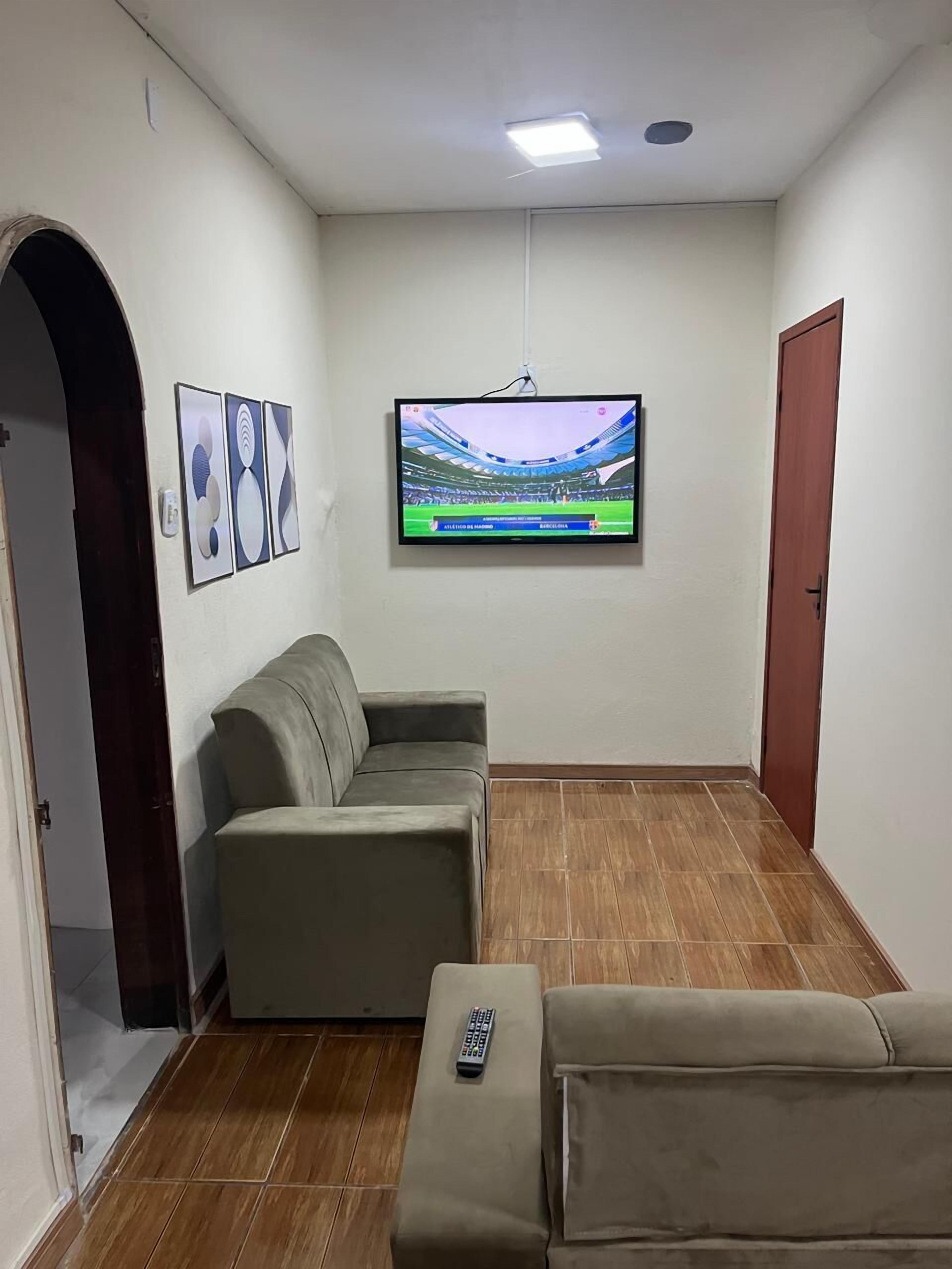 Una habitación con un sofá, un televisor montado en la pared y un control remoto sobre el sofá.