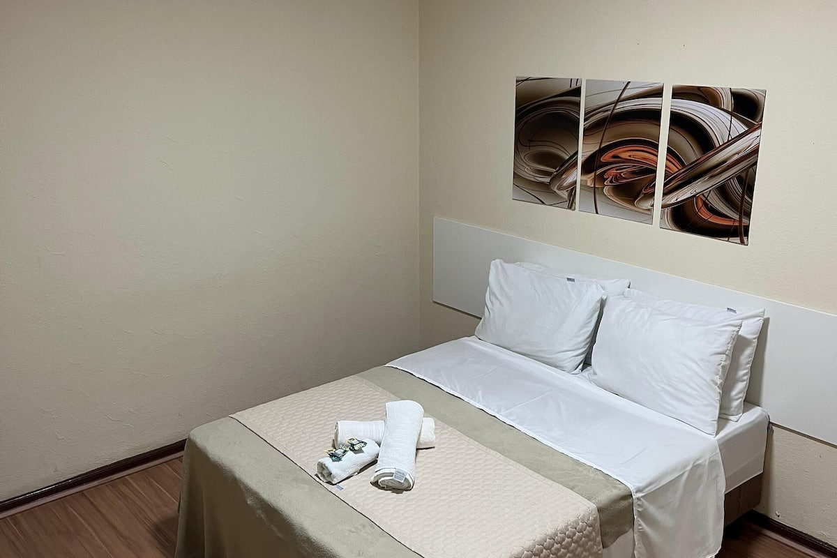 A hotel room with a bed, a table, and a wall-mounted artwork.