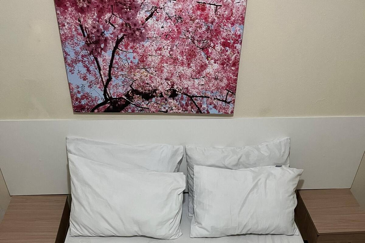 A neatly made bed with white linens, a quilted mattress, and a decorative pillow with a floral pattern.