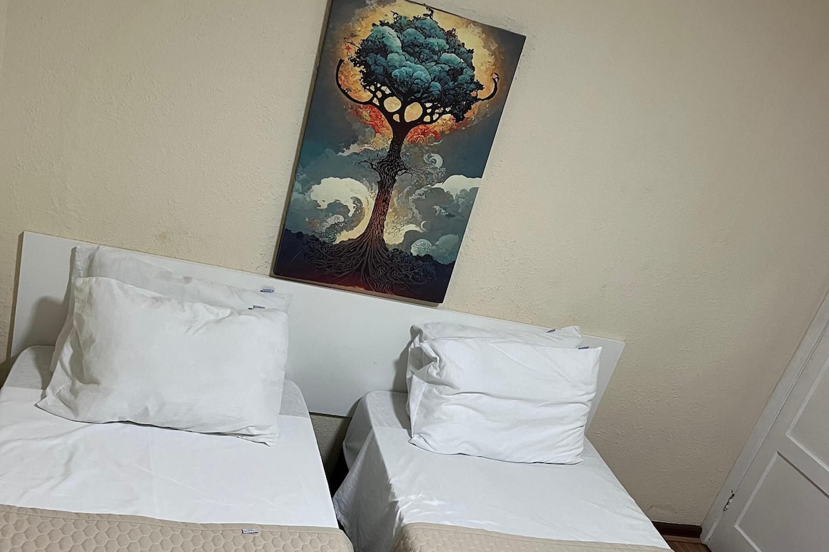 Two beds with white linens, a painting of a tree on the wall, and towels on the floor.