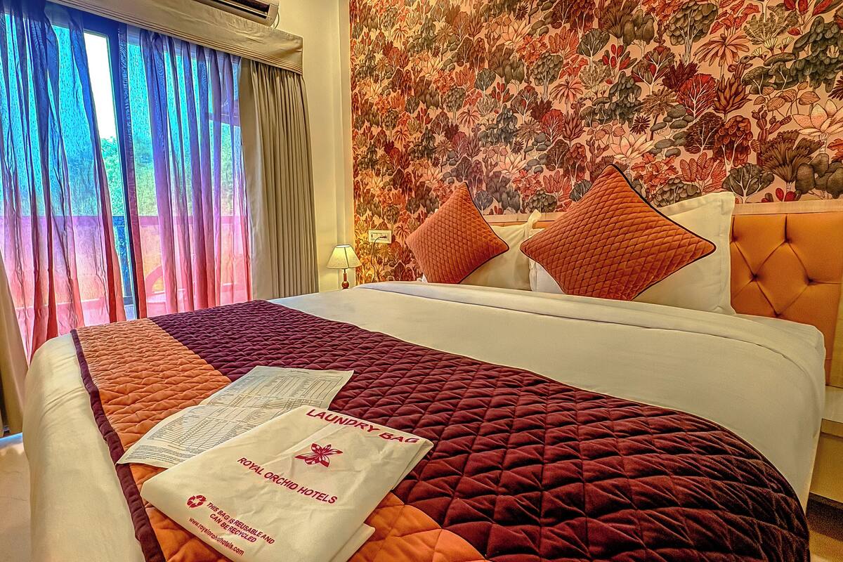 A hotel room with a bed, a floral wallpaper, and a window with curtains.