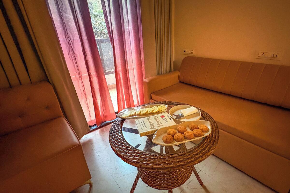 A cozy living area with a sofa, a wicker table with snacks, and a window with curtains.