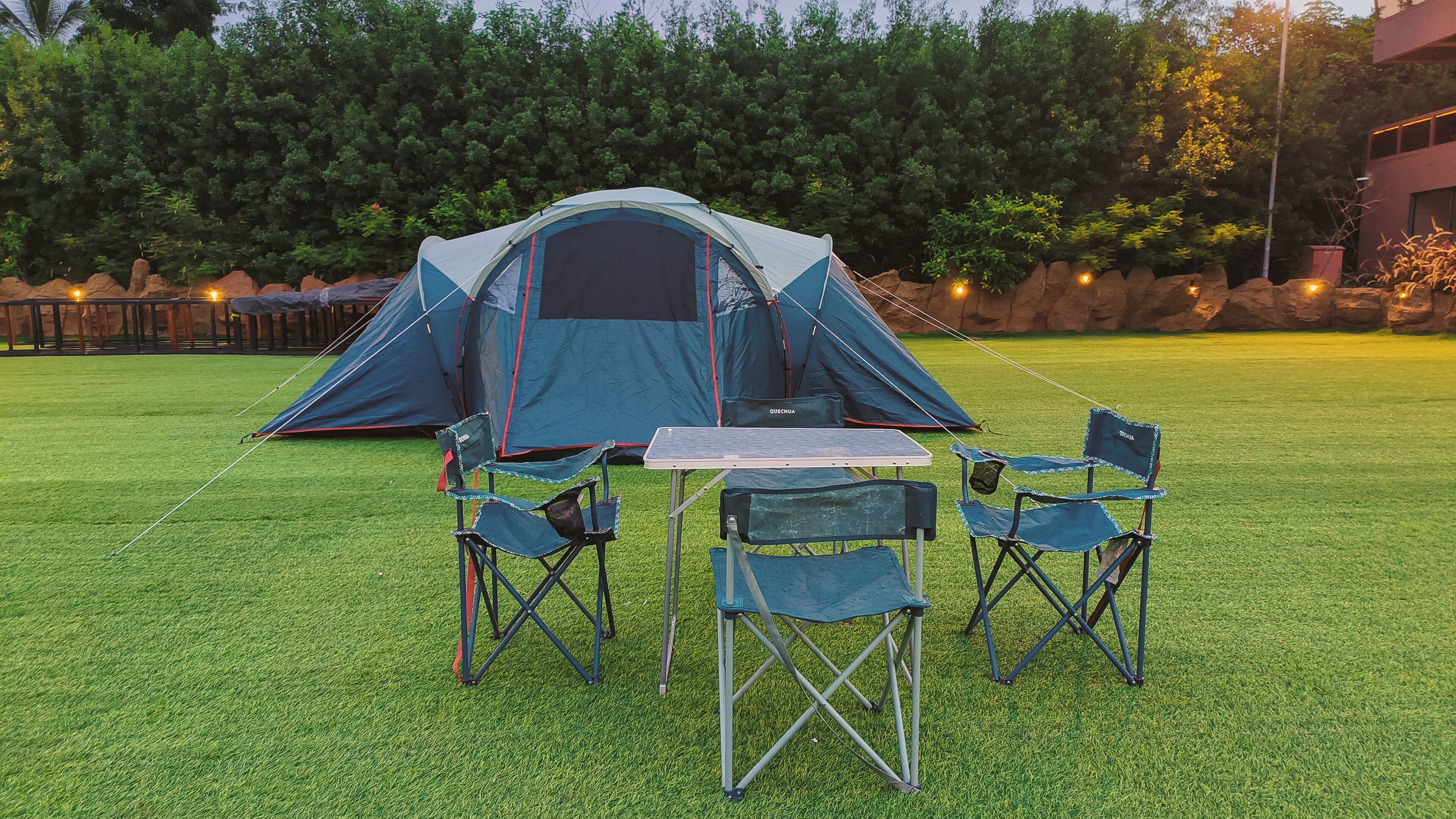 Un espace de camping aménagé avec une tente, une table et deux chaises, le tout installé sur une pelouse artificielle.