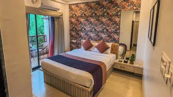 A hotel room with a bed, a bedside table with a lamp, a mirror, and a view of the outdoors.
