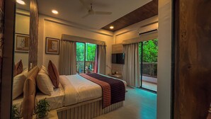 A bedroom with a bed, curtains, a TV, and a view of greenery outside. - Regenta Bharti Amusement & Adventure Resort Pune, Urulikanchan (Daund)
