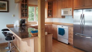Une cuisine moderne avec des meubles en bois, un réfrigérateur en acier inoxydable, un four encastré et un coin bar avec des tabourets.