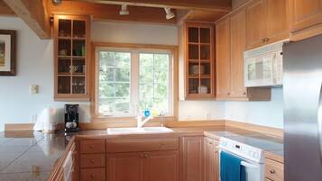 A kitchen with wooden cabinets, a stainless steel refrigerator, a microwave, and a window with a view of greenery.