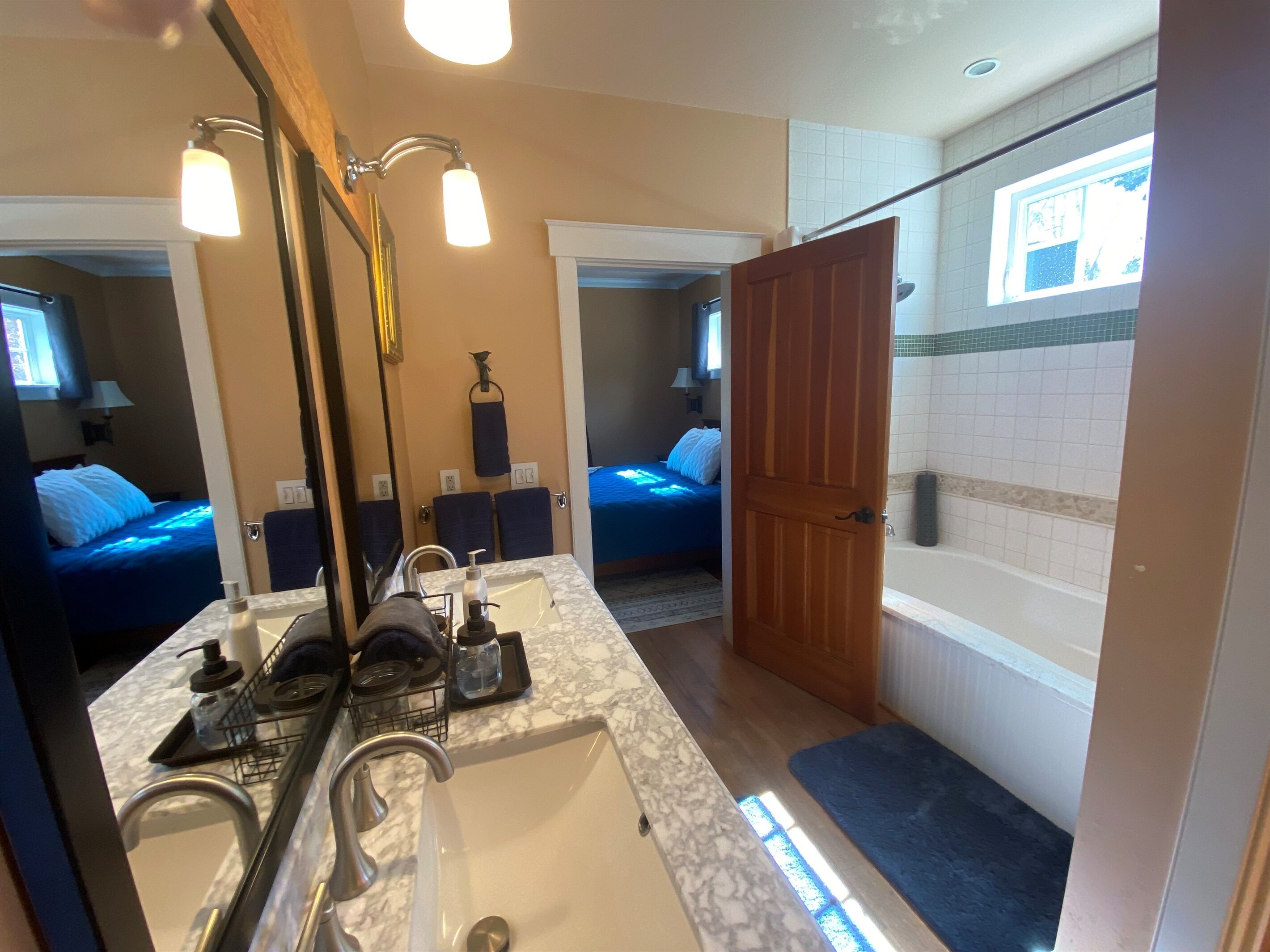 A bathroom with a large mirror, a sink, a shower, and a door leading to a bedroom.