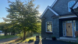 A two-story house with a dark gray exterior, a large window with a white frame, and a wooden door. - The Orchard at Lovers Lane and Enchanted Forest. Hot Tub, Pets Welcome (Eastsound)