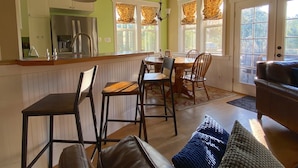 A spacious kitchen with a dining area, wooden chairs, and a large window with curtains. - The Orchard at Lovers Lane and Enchanted Forest. Hot Tub, Pets Welcome (Eastsound)