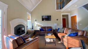 A spacious living room with a fireplace, leather sofas, a coffee table, and a TV mounted on the wall. - The Orchard at Lovers Lane and Enchanted Forest. Hot Tub, Pets Welcome (Eastsound)