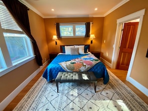 A bedroom with a bed, two bedside lamps, a window with curtains, a door, and a patterned rug. - The Orchard at Lovers Lane and Enchanted Forest. Hot Tub, Pets Welcome (Eastsound)