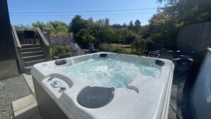 A hot tub with a wooden deck and steps leading up to it, surrounded by greenery and outdoor furniture. - The Orchard at Lovers Lane and Enchanted Forest. Hot Tub, Pets Welcome (Eastsound)