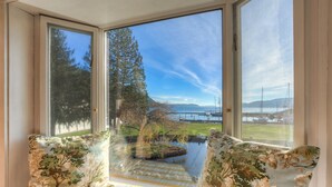 A bay window with a view of a lake, a grassy area, and a tree. - Historic Waterfront Home, Hot tub, Pets Welcome! (Eastsound)