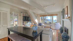 A spacious living area with a dining table, seating, a fireplace, and a view of the outdoors. - Historic Waterfront Home, Hot tub, Pets Welcome! (Eastsound)