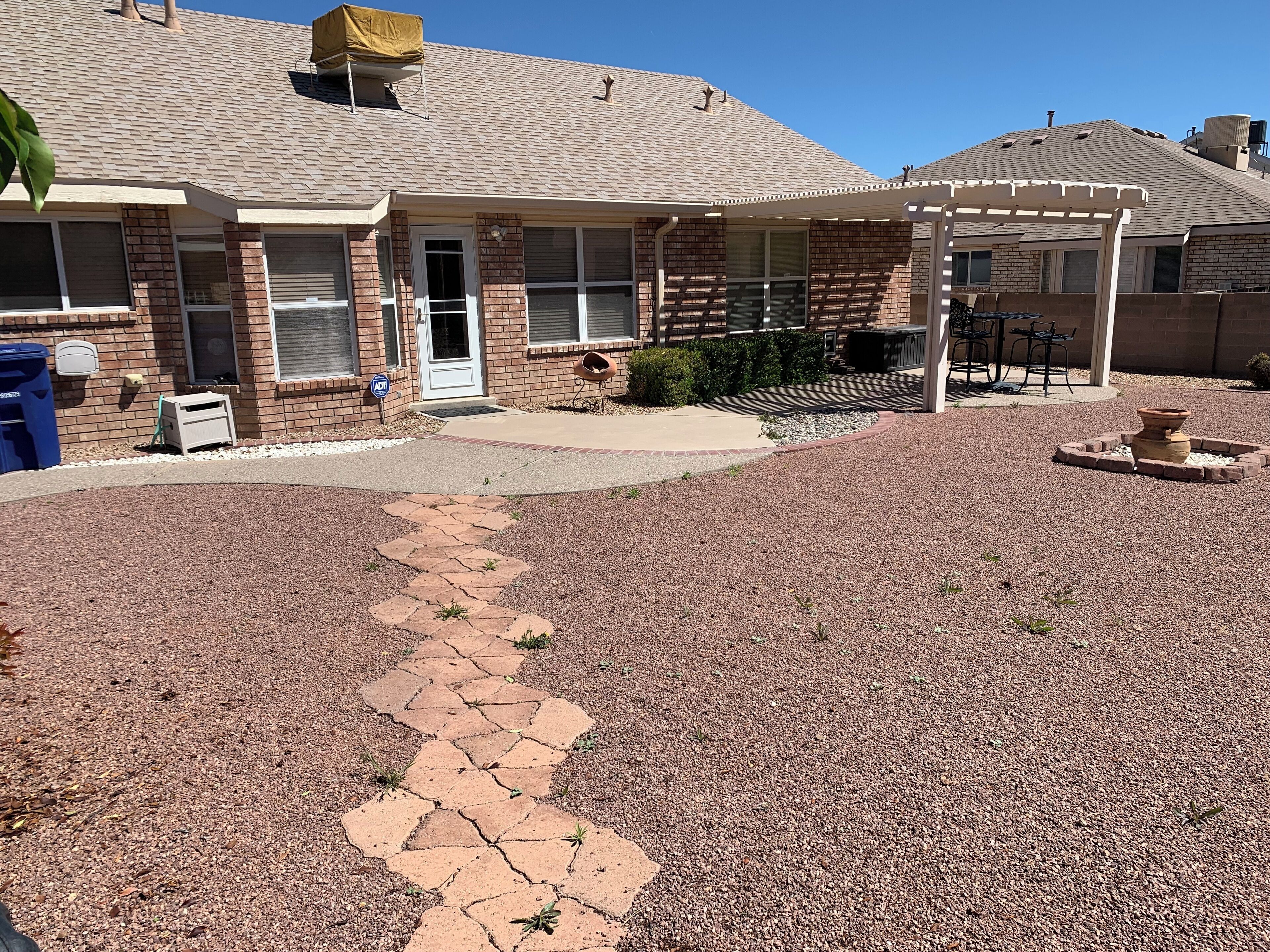 Une maison d’habitation avec une façade en briques, un patio couvert et une allée gravillonnée.