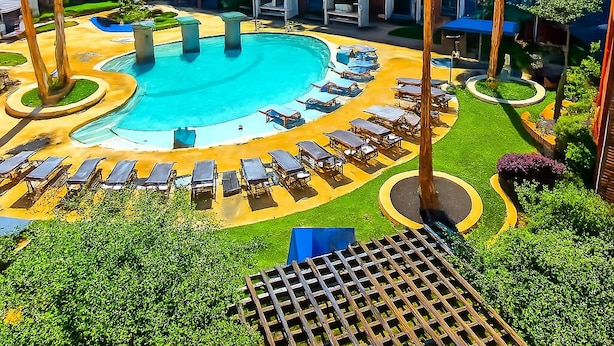 A hotel with a swimming pool surrounded by lounge chairs and palm trees. - Sunshine Stay | 2BR Galleria Apartment Nr Mall (Houston)