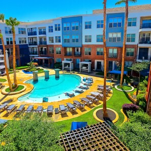 A hotel with a swimming pool surrounded by lounge chairs and palm trees. - Sunshine Stay | 2BR Galleria Apartment Nr Mall (Houston)