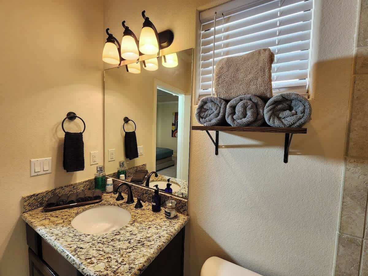 A bathroom with a granite countertop sink, a mirror, and a towel rack with towels.