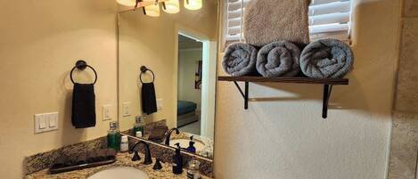 A bathroom with a granite countertop sink, a mirror, and a towel rack with towels.